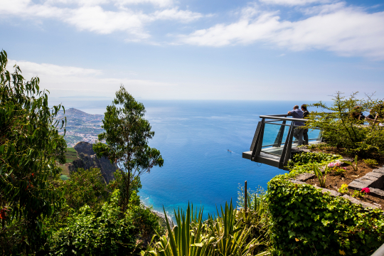 Blick von der Seite auf den ber&uuml;hmten Skywalk auf Madeira, zwei Personen von der Seite zu sehen und ein weiter Blick &uuml;ber die K&uuml;ste