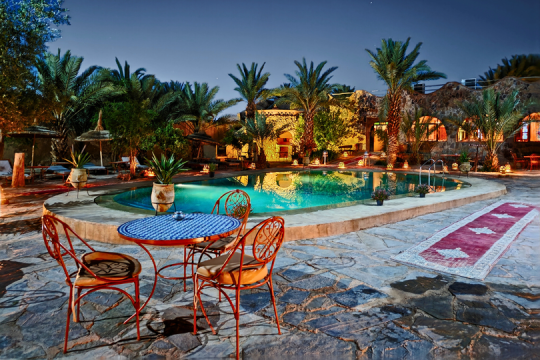 Tisch mit zwei Stühlen an einem Hotelpool, kleine Hotelanlage bei Nacht